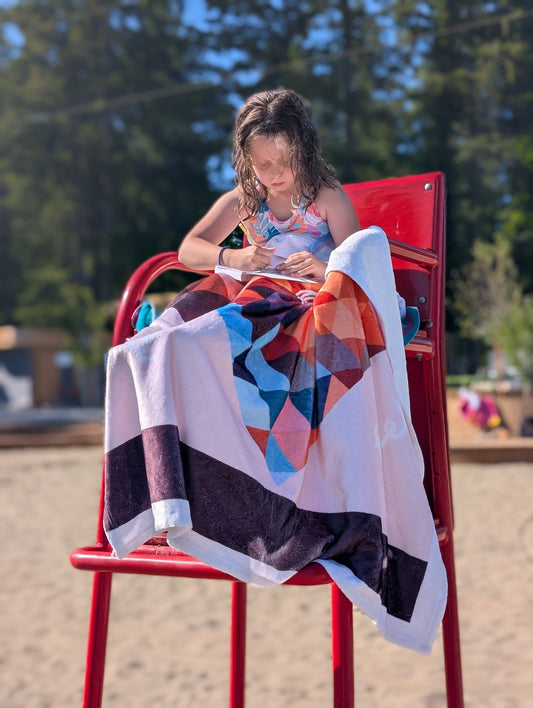 Colorful geometric-patterned communication blanket draped over a child outdoors. The blanket features a communication tool printed in the design. 