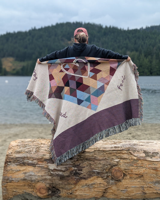 Person holding a geometric-patterned blanket by a lake. Blanket features emotional regulation steps printed into the design. 